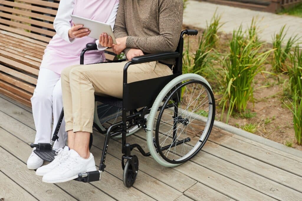 person in a wheelchair outside next to wooden garden bench 